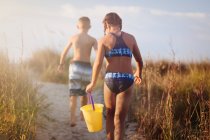 Rear view of girl and boy walking over grassy dune, North Myrtle Beach, South Carolina, United States, North America — Stock Photo