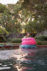 Menina em anéis infláveis sentados no lado da piscina exterior — Fotografia de Stock
