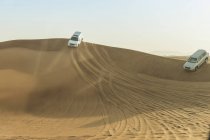 Внедорожники едут по пустынным дюнам, Дубай, ОАЭ — стоковое фото