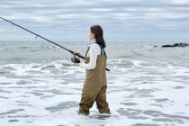 Молодая женщина в вадерах рыбачит в воде — стоковое фото