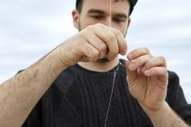 Young man attaching fishing hook to fishing line — Stock Photo