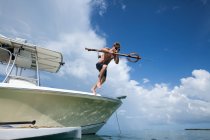Человек, прыгающий в воду с лодки, несущий рыбацкое копье — стоковое фото