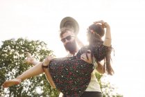 Young man carrying boho girlfriend in arms at festival outdoors — Stock Photo