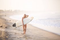 Portrait of young female surfer carrying surfboard along beach, Santa Monica, California, USA — Stock Photo