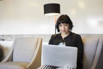 Середня доросла жінка сидить у кріслі і використовує ноутбук — стокове фото