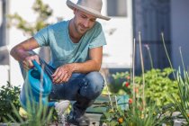 Молодой человек поливает растения в саду — стоковое фото