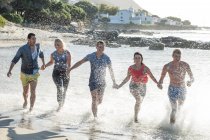Jovens amigos adultos correndo e salpicando através de ondas na festa na praia — Fotografia de Stock