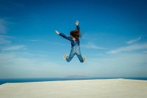 Vue arrière de la jeune fille sautant en plein air avec la mer en arrière-plan, Santorin, Kikladhes, Grèce — Photo de stock