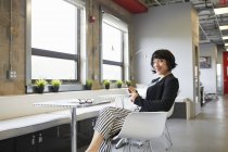 Retrato de mujer de negocios sentada a la mesa en la oficina con smartphone - foto de stock