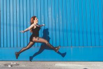 Mulher na frente da parede azul pulando no ar — Fotografia de Stock