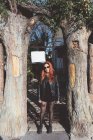 Portrait of red haired woman in sunglasses standing between trees — Stock Photo