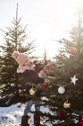 Chica poniendo bolas en el árbol de navidad del bosque - foto de stock