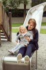 Madre e figlia bambino su scivolo parco giochi — Foto stock