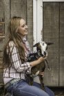 Portrait of young woman holding goat, smiling — Stock Photo