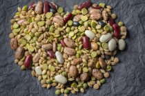 Beans and nuts lay out in form of heart on gray background — Stock Photo