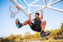 Junger Mann auf Basketballplatz schwingt auf Basketballnetz — Stockfoto