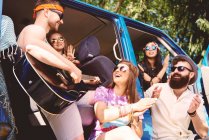 Fünf junge erwachsene Freunde spielen Akustikgitarre und klatschen im Freizeitbus — Stockfoto