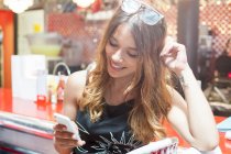 Молодая женщина сидит в кафе, смотрит на смартфон, улыбается — стоковое фото