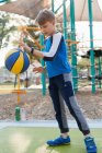 Молодий хлопчик підстрибує баскетбол на дитячому майданчику — стокове фото