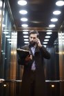 Young businessman in elevator making smartphone call — Stock Photo