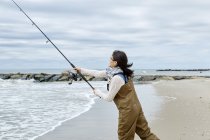 Young woman casting fishing rod from beach — Stock Photo