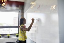 Jovem mulher escrevendo em quadro branco no ambiente de escritório — Fotografia de Stock