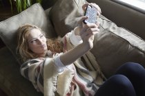 Jovem mulher tomando selfie no sofá — Fotografia de Stock