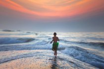 Junge läuft bei Sonnenuntergang ins Meer, North Myrtle Beach, South Carolina, Vereinigte Staaten — Stockfoto