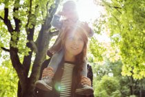 Madre dando figlia bambino sulle spalle nel parco illuminato dal sole — Foto stock