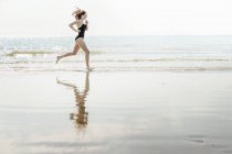 Vista lateral da jovem correndo na praia — Fotografia de Stock