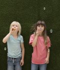 Due bambini di fronte a parete in erba artificiale soffiando bolle — Foto stock