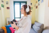 Jovem mulher na sala de estar ouvindo música smartphone em fones de ouvido — Fotografia de Stock