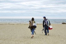 Giovane coppia che trasporta attrezzature da pesca sulla spiaggia — Foto stock