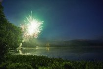 Fogos de artifício explodindo sobre o lago ao anoitecer — Fotografia de Stock