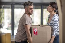 Couple dans une maison non meublée portant une boîte de biens fragiles — Photo de stock