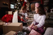 Молода дівчина і хлопчик сортують різдвяні подарунки, список прокату молодого хлопчика — стокове фото