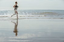 Вид зрелой женщины, бегущей по пляжу сбоку — стоковое фото