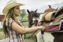 Mujer joven en la granja, caballo ensillado - foto de stock