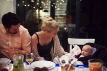 Couple sitting at dinner table, tending to baby daughter — Stock Photo