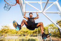 Jeune homme sur le terrain de basket balançant sur le cadre du filet de basket — Photo de stock