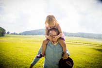 Chica consiguiendo cerdito espalda de padre en campo rural, cubriendo sus ojos - foto de stock
