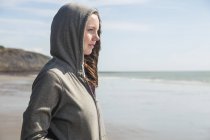 Jovem mulher em top com capuz olhando para a praia — Fotografia de Stock