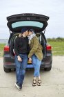 Young couple sitting and kissing in open car trunk — Stock Photo