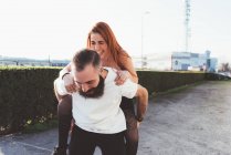 Homem dando vermelho cabelos mulher no piggyback — Fotografia de Stock