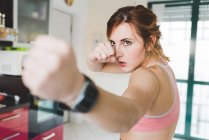 Young woman doing boxing training in kitchen — Stock Photo