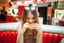 Retrato de jovem sentada no restaurante, comendo sanduíche — Fotografia de Stock