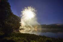 Fogos de artifício explodindo sobre o lago ao anoitecer — Fotografia de Stock