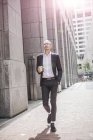 Businessman with takeaway coffee strolling along sidewalk — Stock Photo