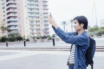 Vista lateral del joven tomando fotos con el teléfono inteligente - foto de stock