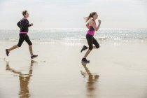 Side view of mother and daughter running on beach — Stock Photo